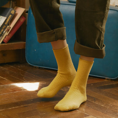 Person wearing yellow socks with rolled-up green pants on a wooden floor.