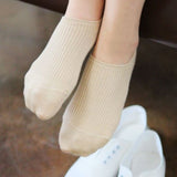 Beige socks worn with white shoes on a wooden floor.