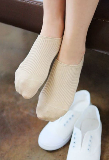 Beige socks worn with white shoes on a wooden floor.