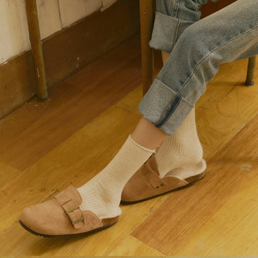 Person wearing brown shoes and beige socks on a wooden floor.