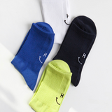 Four socks in blue, white, black, and yellow with smiley face designs on a light gray background.
